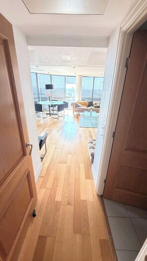 Ein großzügiger Wohnbereich mit hoher Decke, Holzdielen und großen Fenstern mit Blick auf die Stadt.