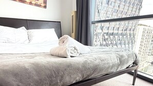 Een hotelkamer met een bed, een wandairconditioner en uitzicht op een modern gebouw door een raam.