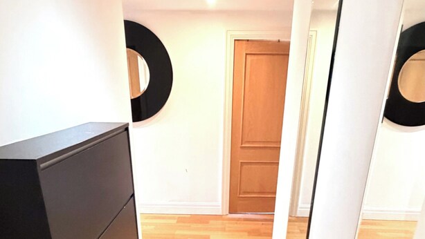 Een hal met een houten vloer, een zwarte dressoir en een deur aan het einde.