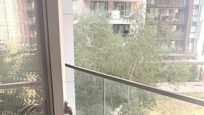 Een balkon met een glazen deur, een metalen hekwerk en uitzicht op een woongebied met bomen en gebouwen.
