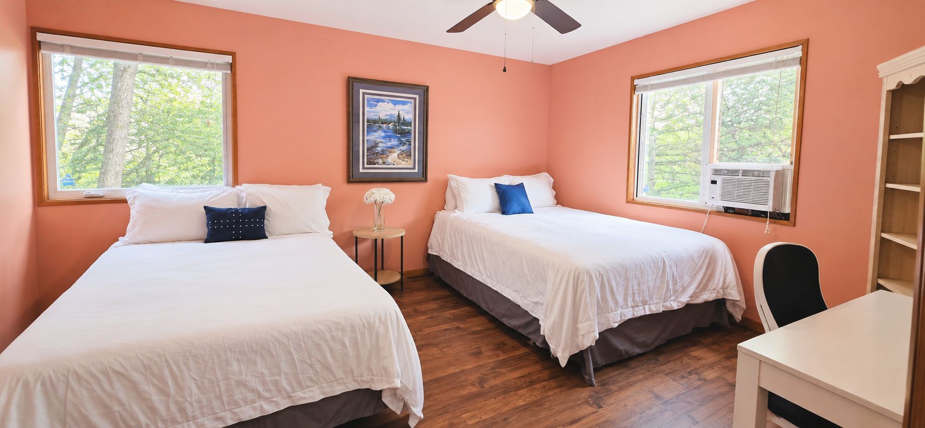 A bedroom with two beds, a ceiling fan, and a window with an air conditioner.
