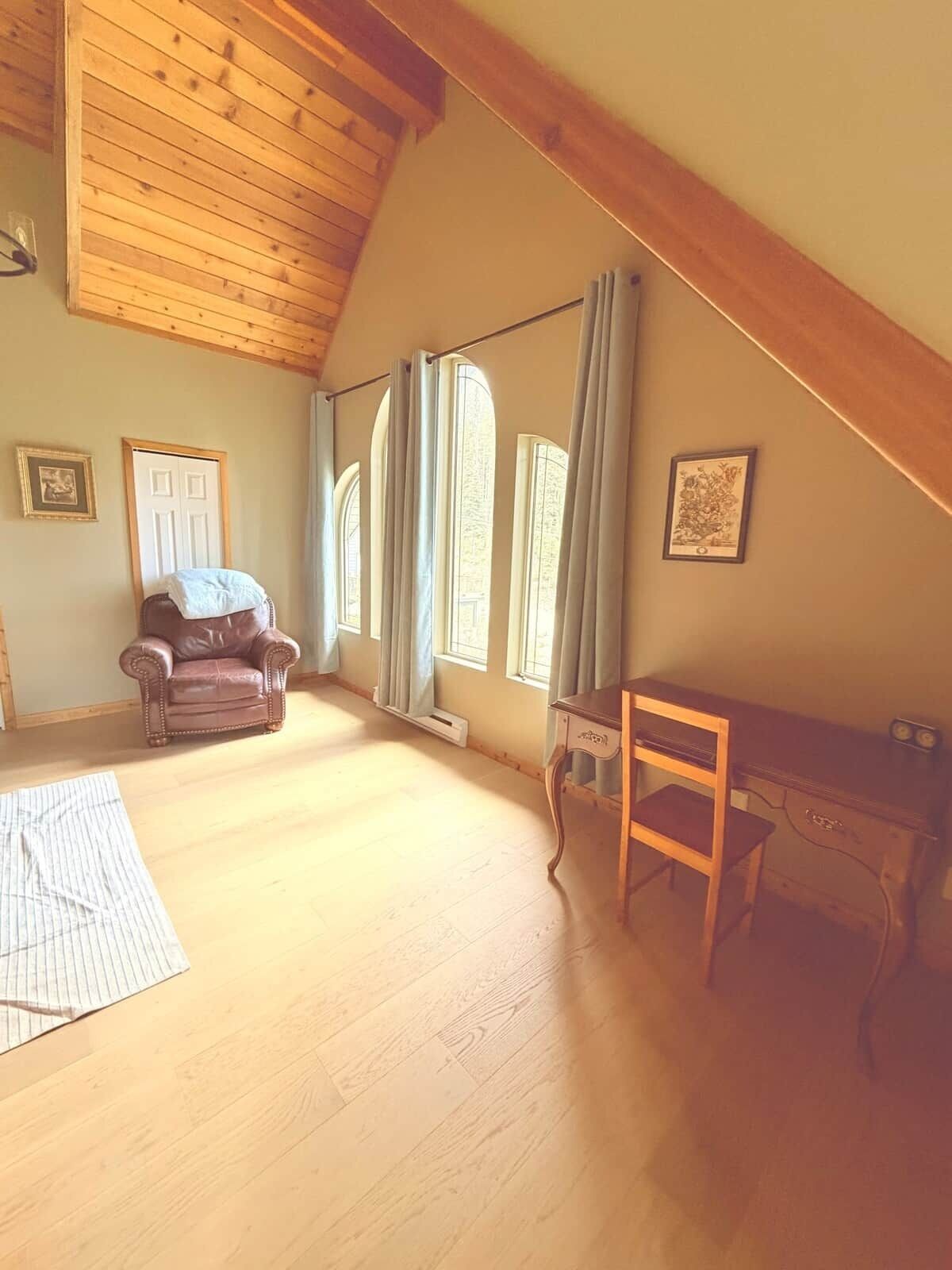 Ein Zimmer mit Holzboden, einem braunen Ledersessel, einem Holztisch und einem Fenster mit Vorhängen.