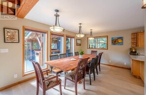 Un comedor con una mesa y sillas de madera, lámparas colgantes y ventanas amplias.
