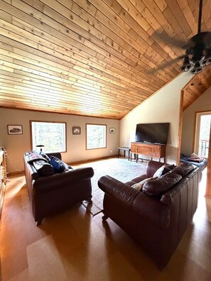 Un loft espacioso con techo inclinado, un ventanal grande, televisor de pantalla plana y chimenea.