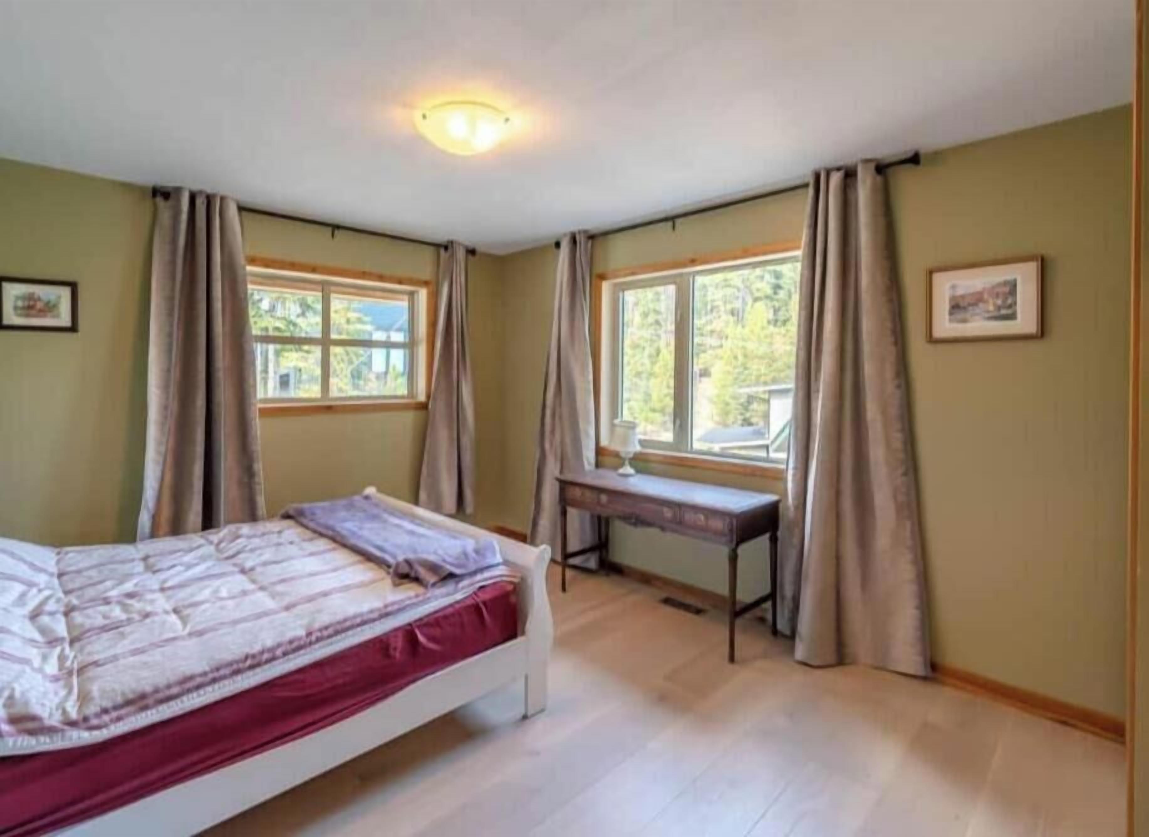 Et soveværelse med en seng, to vinduer, et skrivebord og en bænk.
