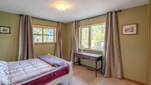 Un dormitorio con cama, dos ventanas, un escritorio y una banca.
