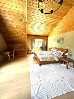 Un dormitorio con techo de madera, una cama, un escritorio y una silla.
