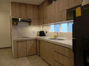 Una cocina con armarios de madera, un lavamanos de acero inoxidable, un refrigerador negro y una ventana que proporciona luz natural.
