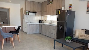 Una cocina moderna con armarios de madera, horno empotrado y refrigerador. Hay un comedor con sillas y una mesa.