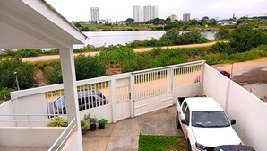 Zona residencial con un edificio blanco, un camino con puerta de acceso, autos estacionados y vista de un río y edificios al fondo.