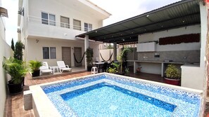 A swimming pool with a tiled edge, surrounded by lounge chairs and potted plants.