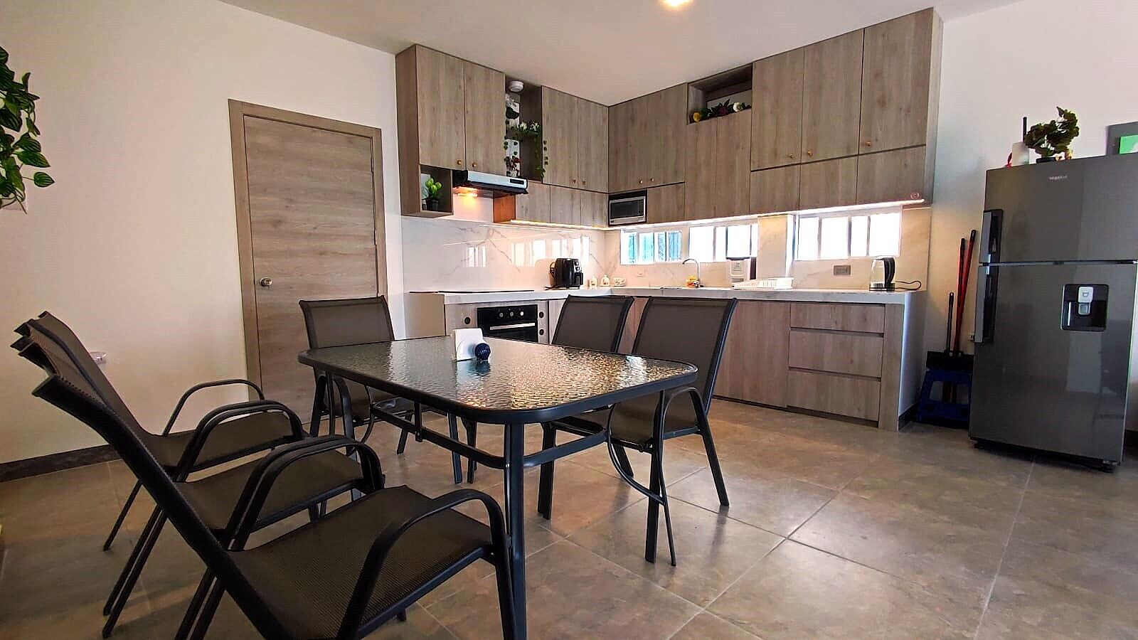 Een moderne keuken met een eettafel en stoelen, houten kastjes, een koelkast en een magnetron.