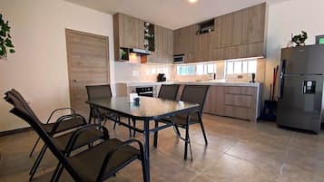 Een moderne keuken met een eettafel en stoelen, houten kastjes, een koelkast en een magnetron.