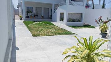 Uma área residencial moderna com um caminho pavimentado, um pequeno espaço gramado e plantas em vasos.