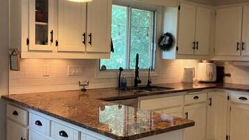 A kitchen with white cabinets, a granite countertop, a window with a view, and pendant lighting.