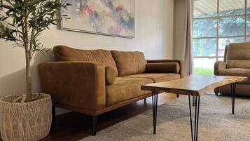 A modern living room with a brown sofa, a wooden coffee table, and a large abstract painting on the wall.