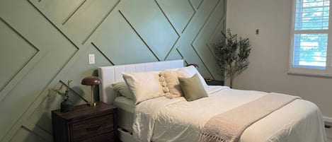 Ein Schlafzimmer mit Bett, Nachttisch, Lampe und Wand mit geometrischer Wandverkleidung.