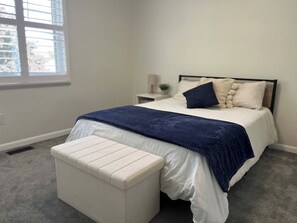 Une chambre à coucher avec un lit, une table de chevet, une lampe et une fenêtre.