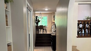 Un couloir avec un escalier menant à une salle à manger, un banc en bois et une plante en pot.
