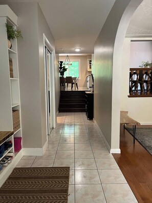 A hallway with a staircase leading to a dining area, a wooden bench, and a potted plant.