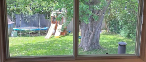 A room with a large window overlooking a backyard with a trampoline and a slide.