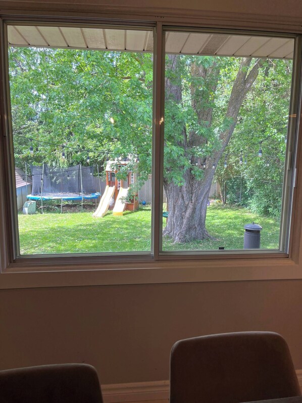 A room with a large window overlooking a backyard with a trampoline and a slide. - Rockway Retreat - Spacious Home & Backyard Oasis (Kitchener)
