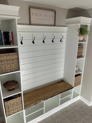 A white built-in bench with a wooden shelf, hooks for hanging items, and wicker baskets.