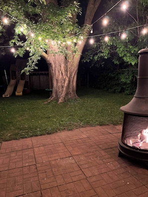 A tree with string lights, a fire pit, and a slide in a backyard.