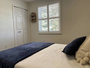 A bedroom with a bed, a window with blinds, a door, and a wall-mounted shelf. - Rockway Retreat - Spacious Home & Backyard Oasis (Kitchener)