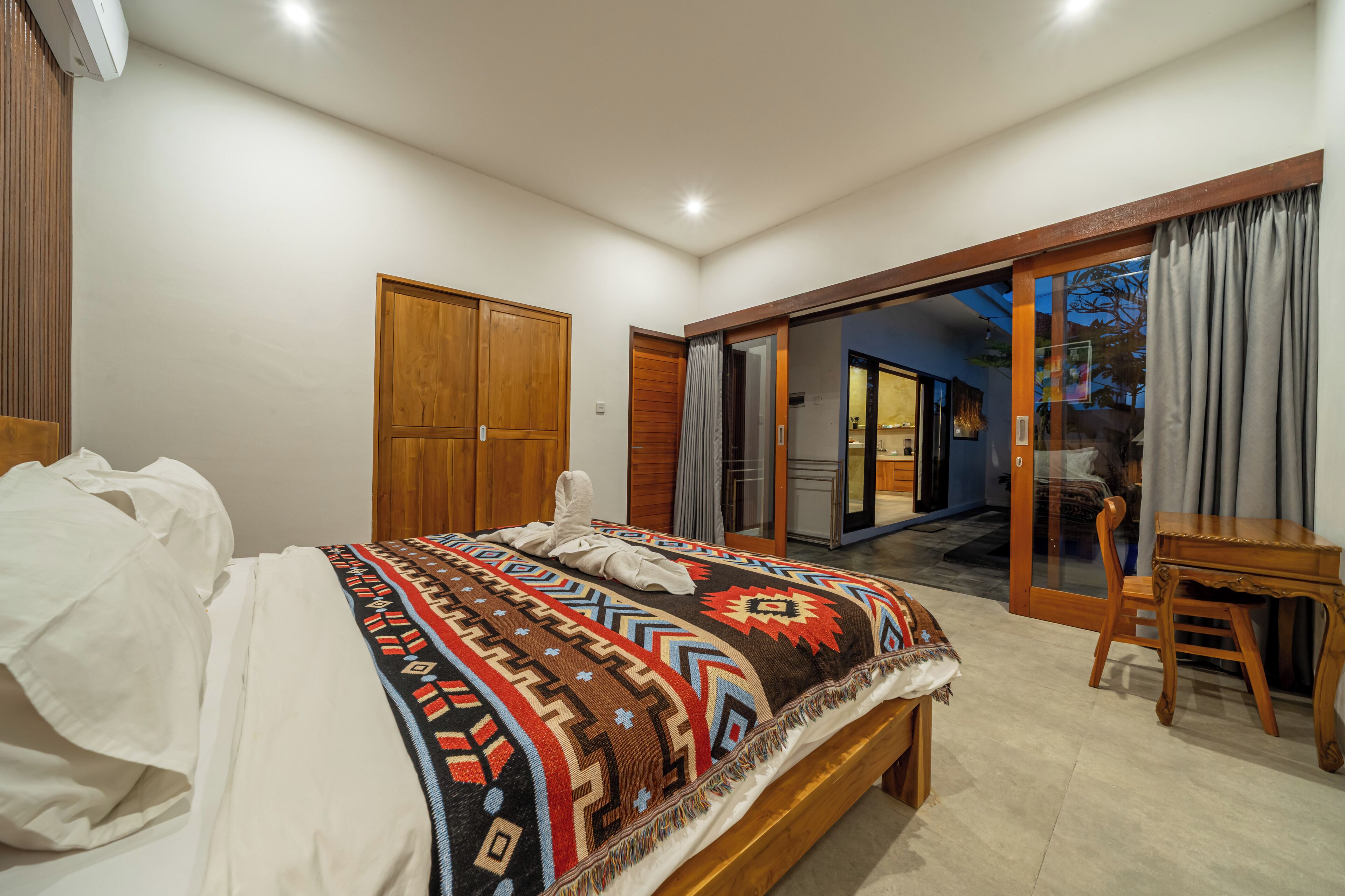 A bedroom with a bed, a wooden wardrobe, a desk, and a sliding glass door leading to an outdoor area.