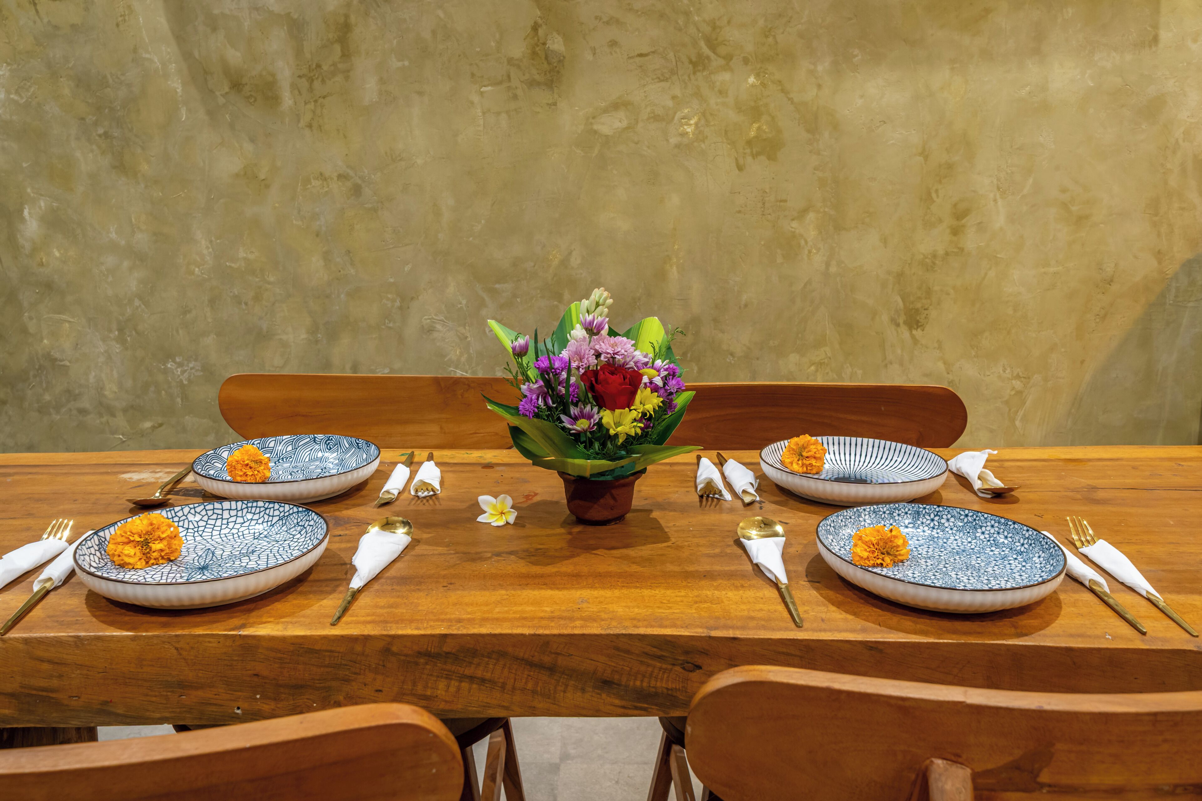 Una mesa de comedor dispuesta con platos de diseño azulado, cubiertos dorados y un centro de mesa con flores.