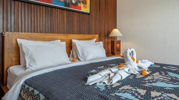 Habitación de hotel con cabecera de madera, edredón estampado, sábanas blancas, un cuadro en la pared y una lámpara de noche.