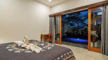 A bedroom with a bed, a wooden chair, and a sliding glass door leading to a pool area.