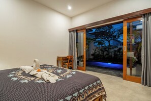 Un dormitorio con cama, una silla de madera y un ventanal corredero que da a una zona de piscina.