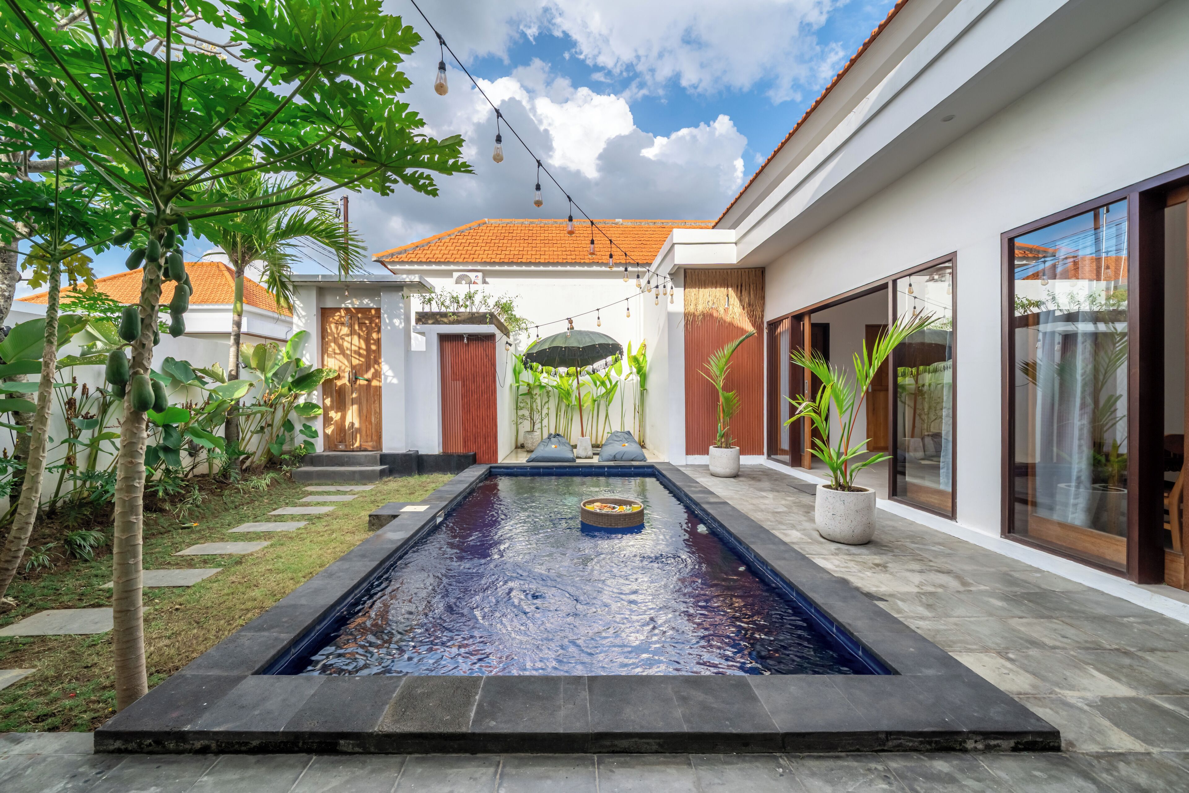A modern house with a swimming pool, outdoor lighting, and potted plants.