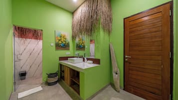 Un baño con pared verde, puerta de madera, lavabo de mármol y un cuadro de flores amarillas.