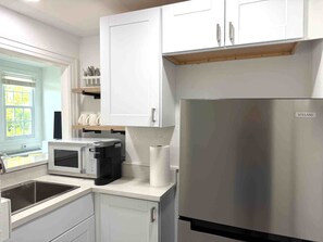 Una cocina moderna con armarios blancos, un refrigerador de acero inoxidable, un microondas y un lavamanos.