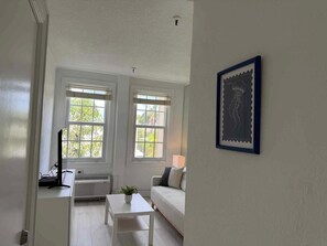 Een kamer met een witte bank, een klein wit tafeltje en twee ramen met witte kozijnen.