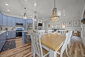 A modern kitchen with blue cabinets, a wooden dining table, and pendant lighting. - Holy Crab!: 4BR 4BA, Pool, Fire Pit, EV Charger, Close to Beach, Sleeps 14 (Oak Island)