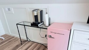 Ett rum med ett skrivbord med glasskiva, ett litet rosa kylskåp och ett vitt skåp med lådor.