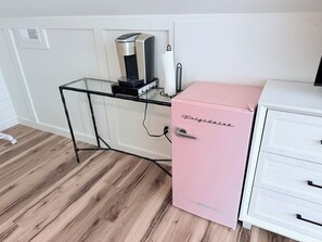 A room with a glass-top desk, a pink mini-fridge, and a white cabinet with drawers. - Holy Crab!: 4BR 4BA, Pool, Fire Pit, EV Charger, Close to Beach, Sleeps 14 (Oak Island)