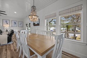 Un coin repas avec une table en bois et des chaises blanches, un lustre et des œuvres d’art encadrées accrochées au mur.