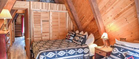 Un dormitorio cálido en el ático con dos camas, paredes de madera y techo inclinado.