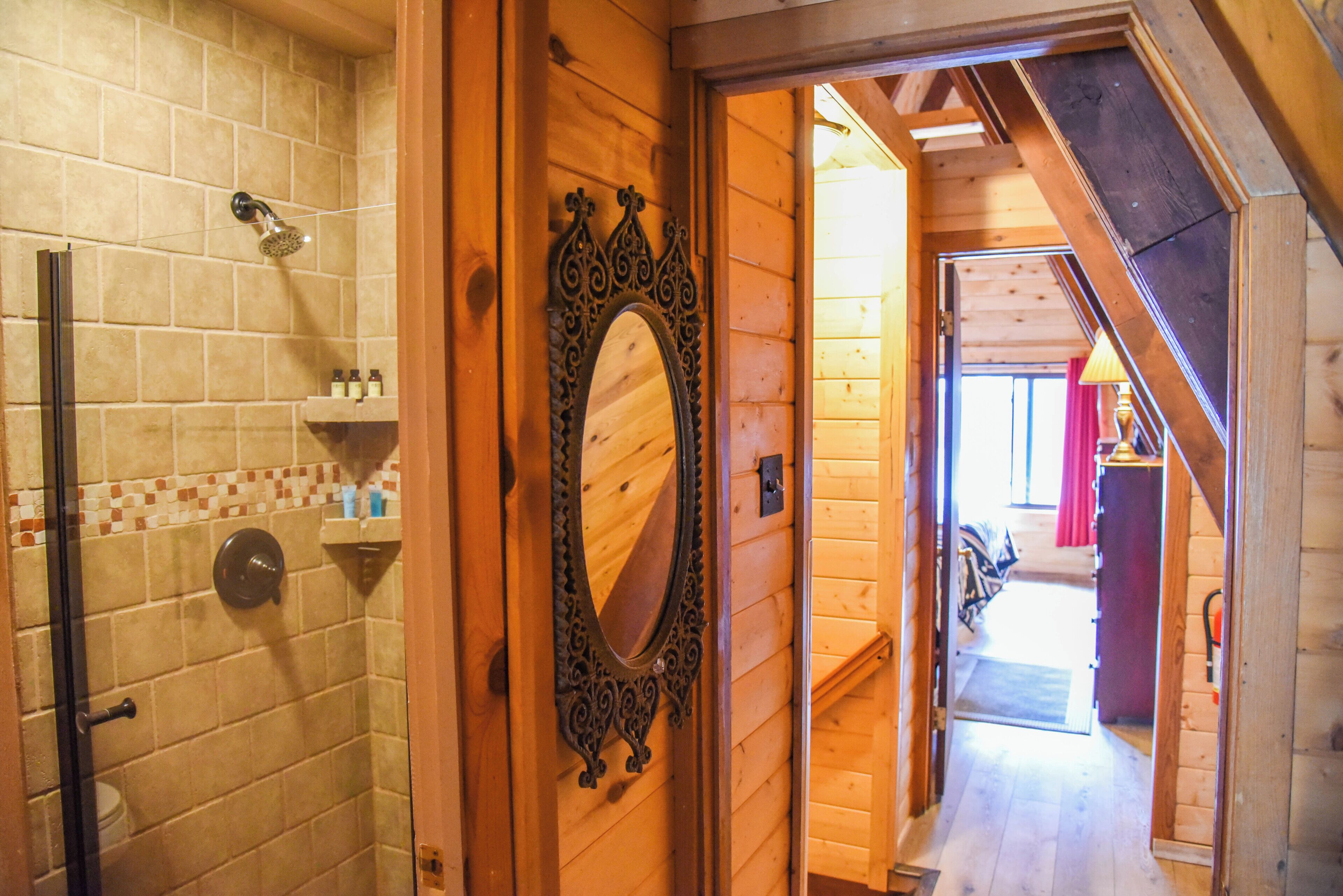 A wooden interior with a shower, a mirror, and a hallway leading to another room.