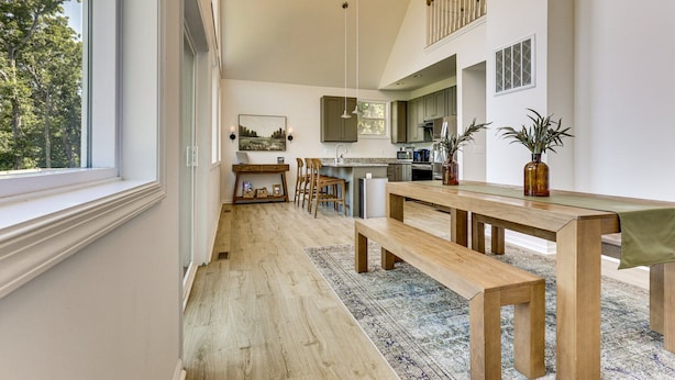 Een ruime keuken met een eethoek, houten vloeren en uitzicht door een groot raam.