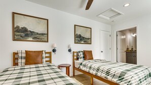 Een kamer met twee bedden, elk met een geruit beddegoed, een nachtkastje, een wandlamp en twee landschapsprenten.