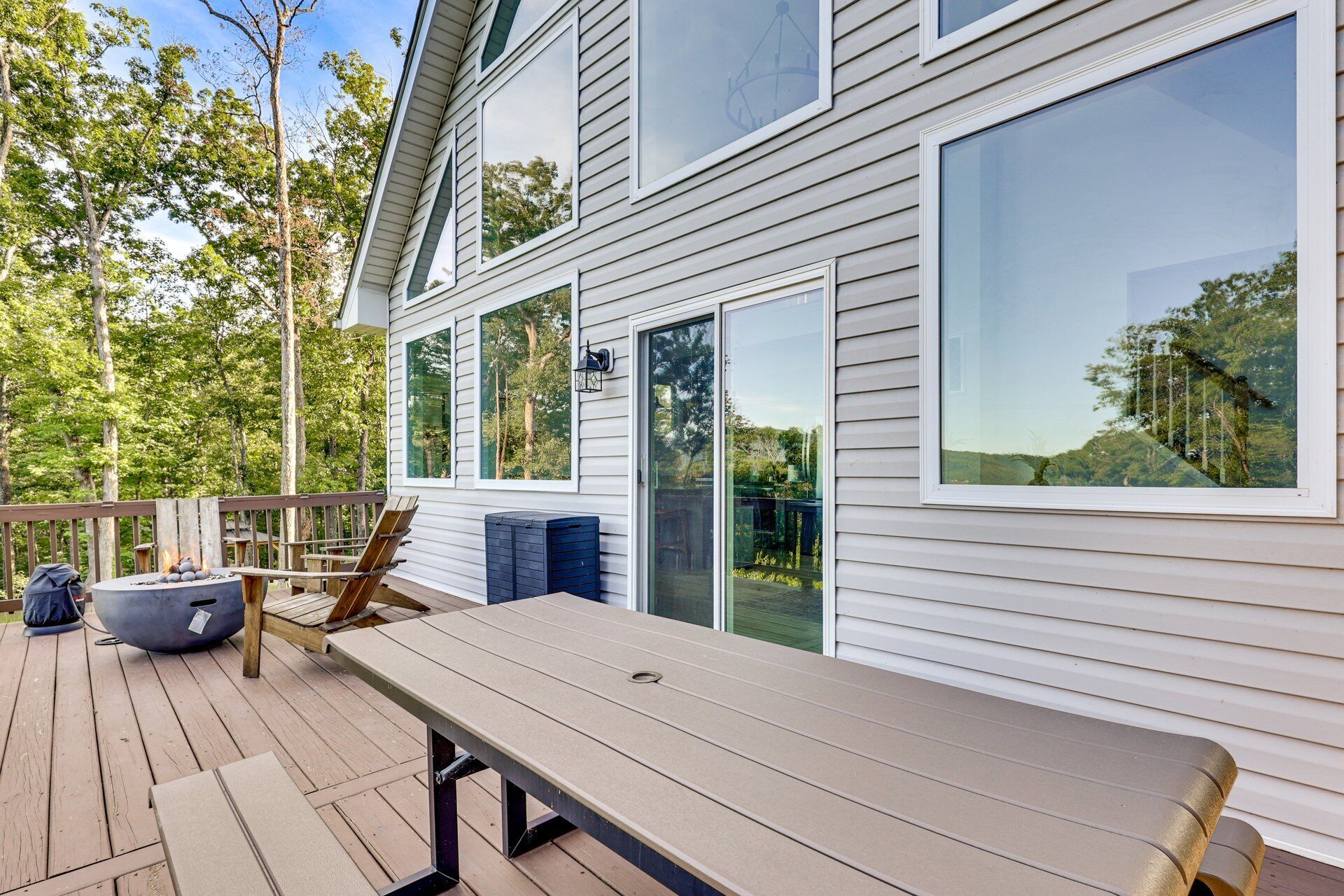 A deck with a table and chairs, a grill, and a large window overlooking a forested area.