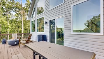 A deck with a table and chairs, a grill, and a large window overlooking a forested area.