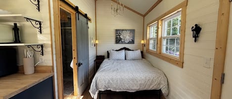 A bedroom with a bed, a wooden floor, a window, and a door leading to a bathroom.