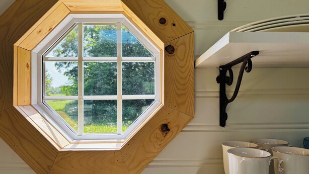 Una ventana de madera hexagonal con vistas a la vegetación.